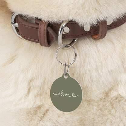 Olive green personalized pet tag on a brown collar against fluffy cream dog fur