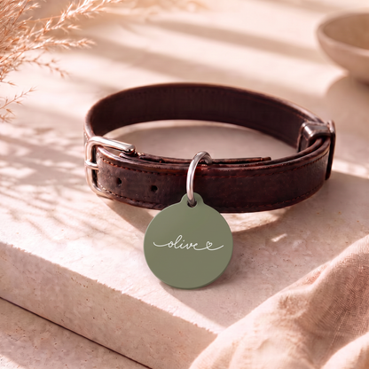 Olive green personalized pet tag on a dark leather collar resting on a table