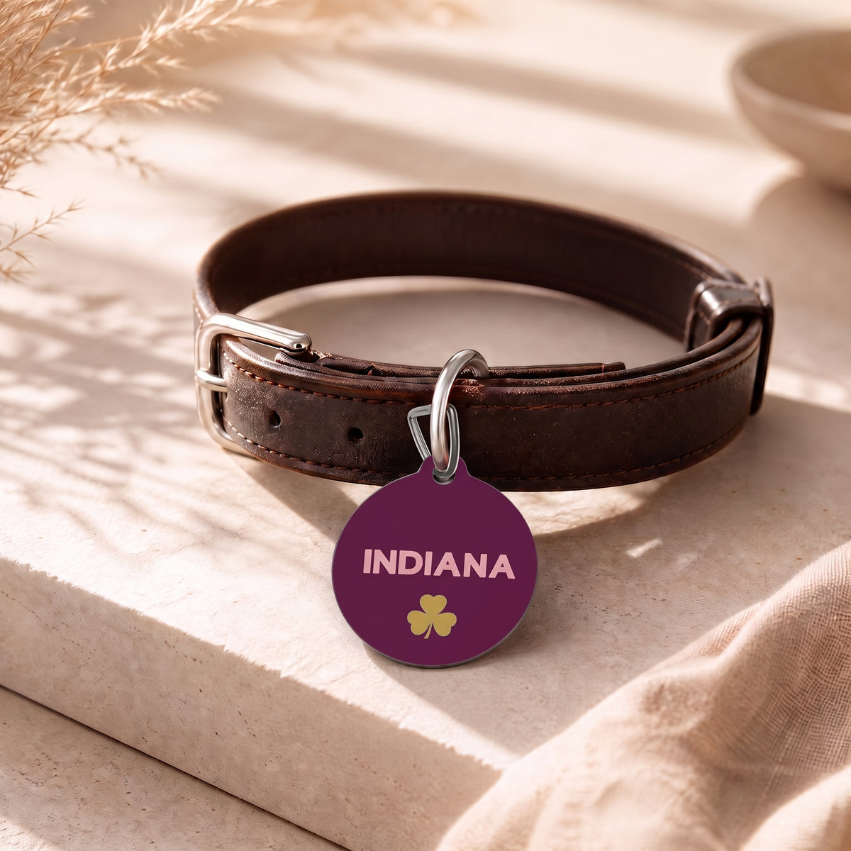 Burgundy clover pet ID tag hanging from a dark brown leather dog collar