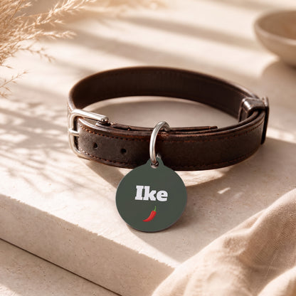Green chili pepper pet ID tag hanging from a dark brown leather dog collar