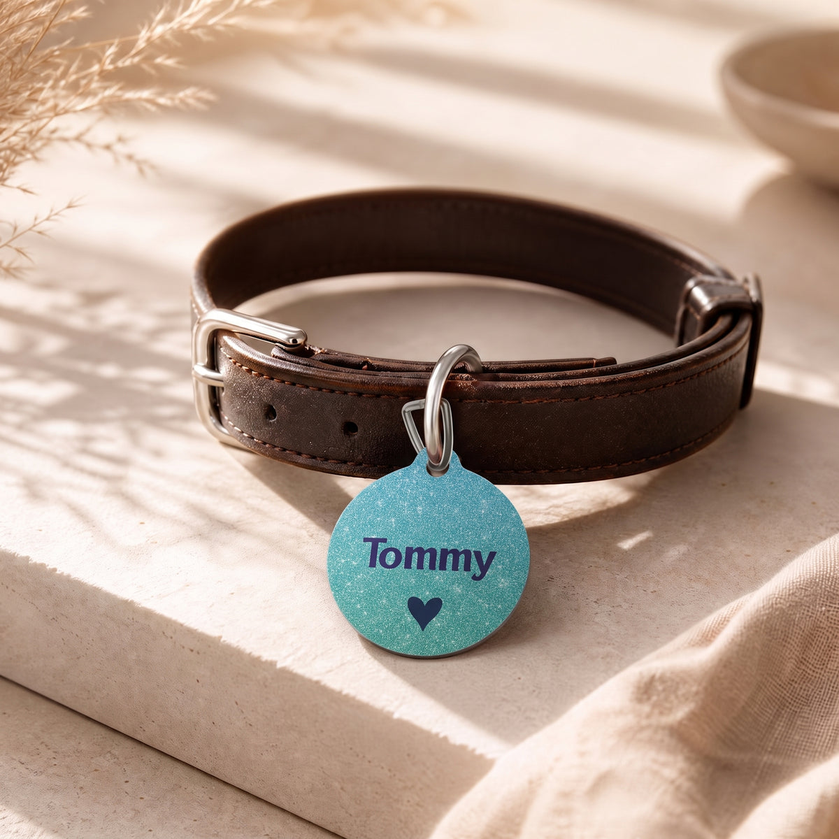 Teal pet ID tag hanging from a dark brown leather dog collar