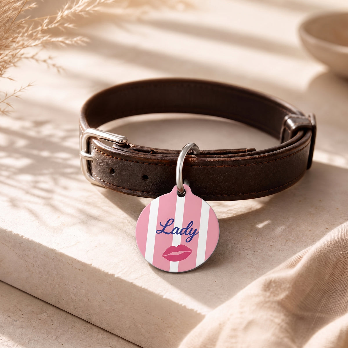 Pink striped pet ID tag hanging from a dark brown leather dog collar