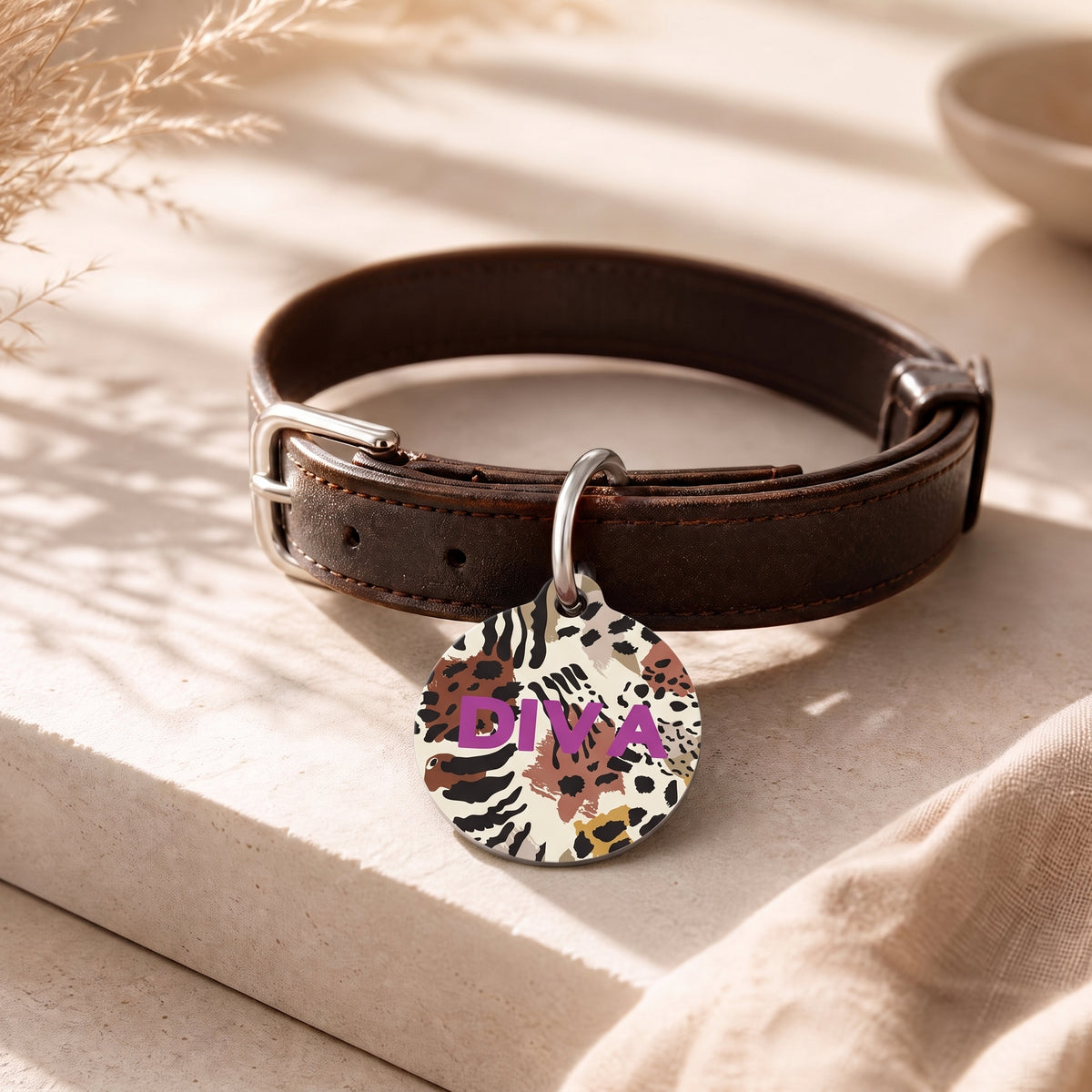 Animal print pet ID tag hanging from a dark brown leather dog collar