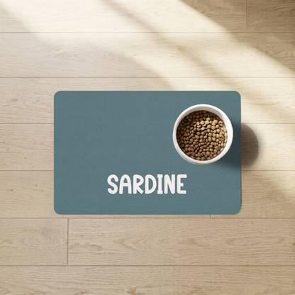 Petrol blue personalized pet food mat with the name Sardine and a food bowl in a sunlit room
