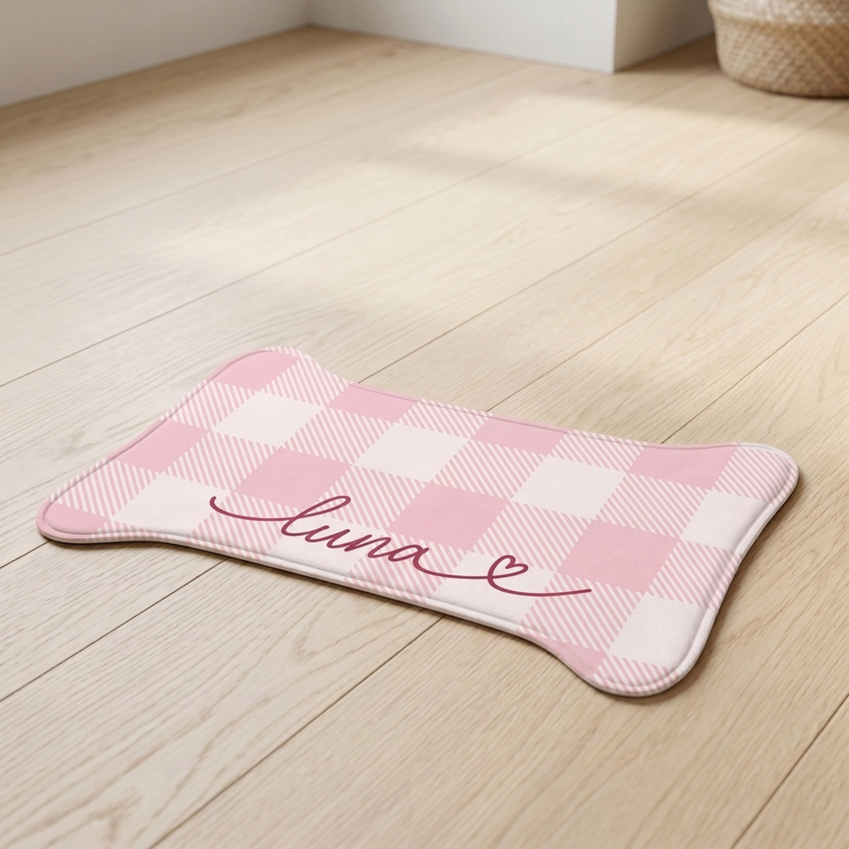 Pink checkered bone-shaped personalized pet feeding mat with the name Luna on a wooden floor