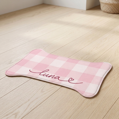 Pink checkered bone-shaped personalized pet feeding mat with the name Luna on a wooden floor