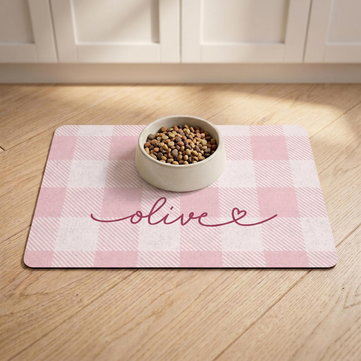 Pink checkered personalized pet food mat with a food bowl on a wooden floor