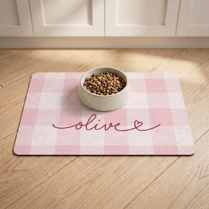 Pink checkered personalized pet food mat with a food bowl on a wooden floor
