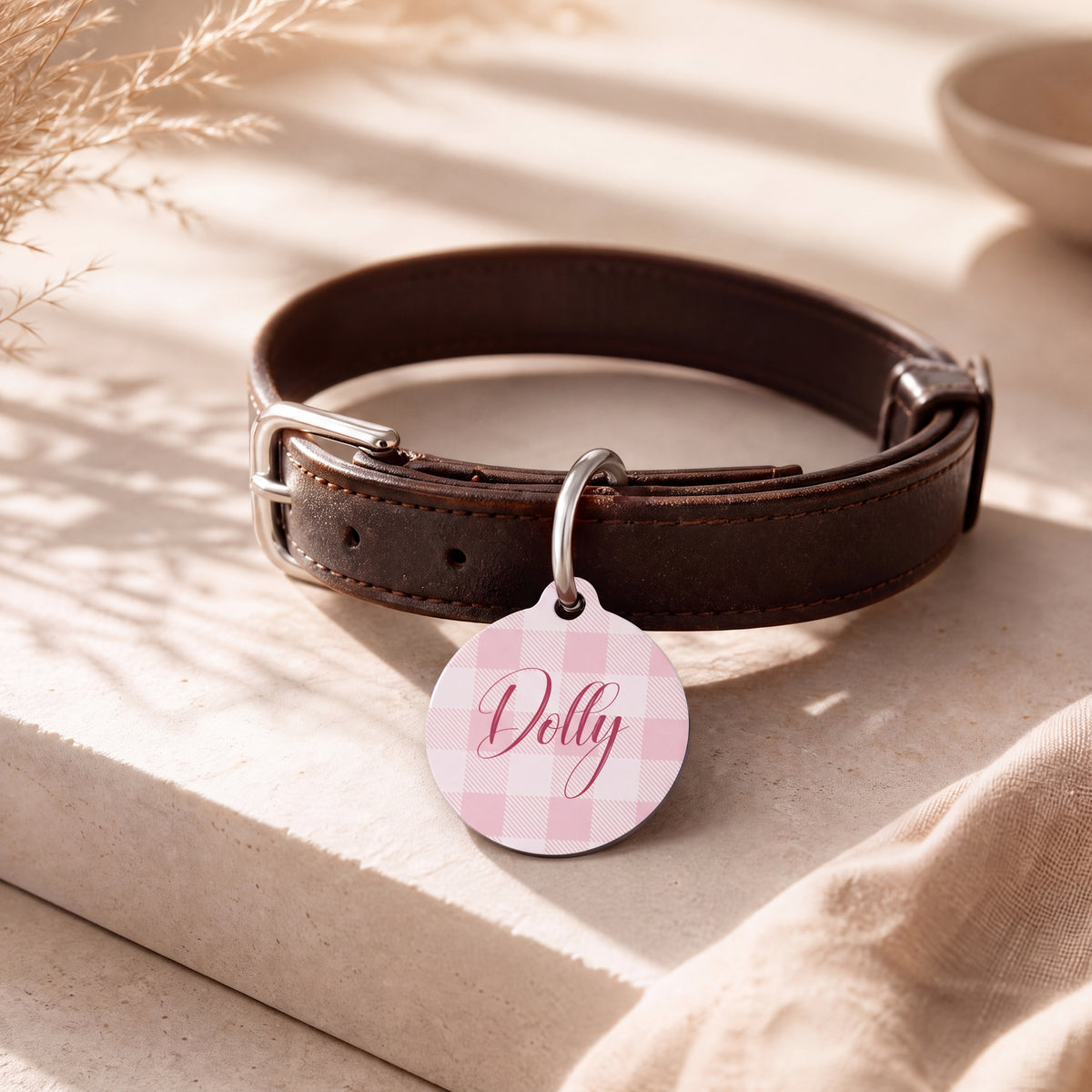 Pink checkered pet tag hanging from a dark brown leather dog collar