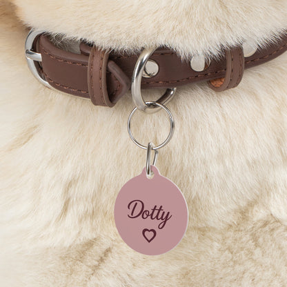 Close-up of the pink heart pet tag hanging from a brown collar on a fluffy dog