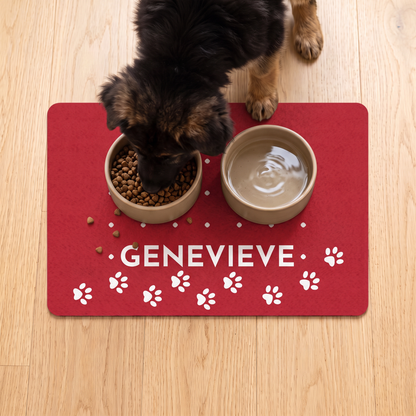 Dog eating from a bowl on a red personalized dog food mat with the name Genevieve and paw prints