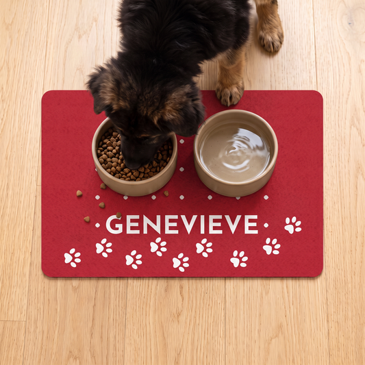 Dog eating from a bowl on a red personalized dog food mat with the name Genevieve and paw prints