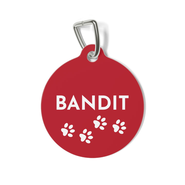 Round red personalized dog tag with the name Bandit in white letters and small white paw prints