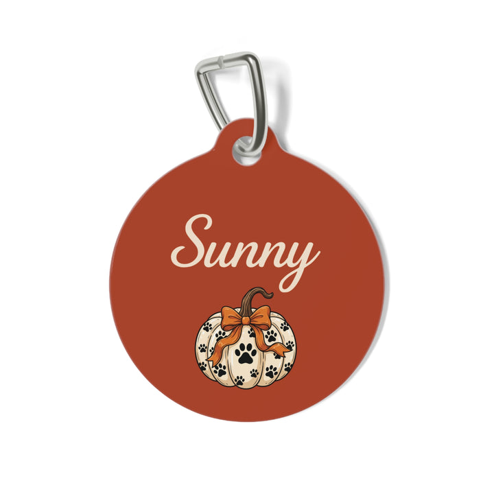 Round rust personalized dog tag with cream script name and a white paw print pumpkin tied with an orange bow