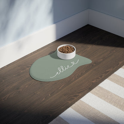 Sage green fish-shaped personalized feeding mat with a bowl on a dark wooden floor