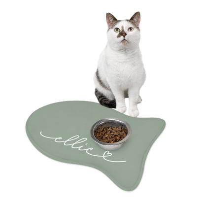 Black and white cat sitting on a sage green fish-shaped personalized feeding mat with a food bowl