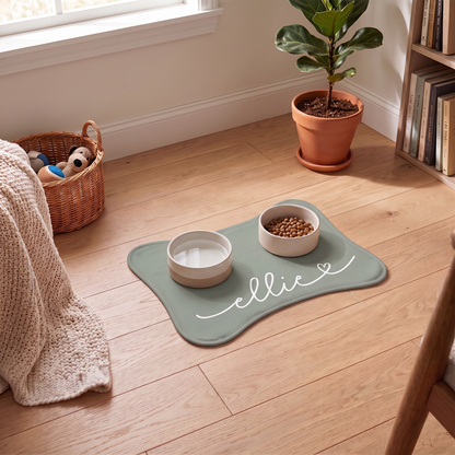 Sage green bone-shaped personalized feeding mat with two bowls in a cozy living room with a plant