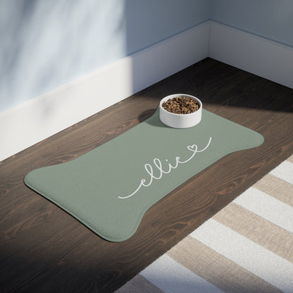 Large sage green bone-shaped personalized feeding mat with a bowl in a sunlit room on a dark wooden floor