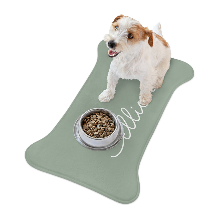 Jack Russell terrier sitting on a sage green bone-shaped personalized feeding mat next to its food bowl