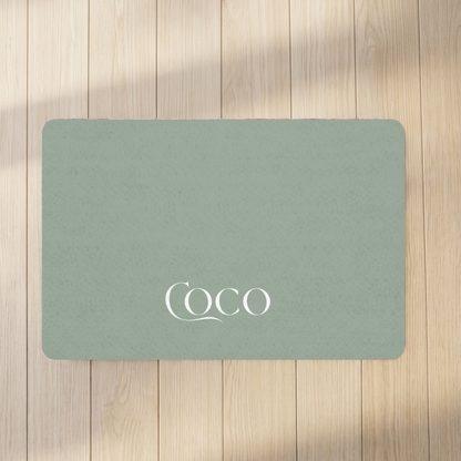 Soft sage personalized pet food mat with the name Coco on a sunlit wooden floor