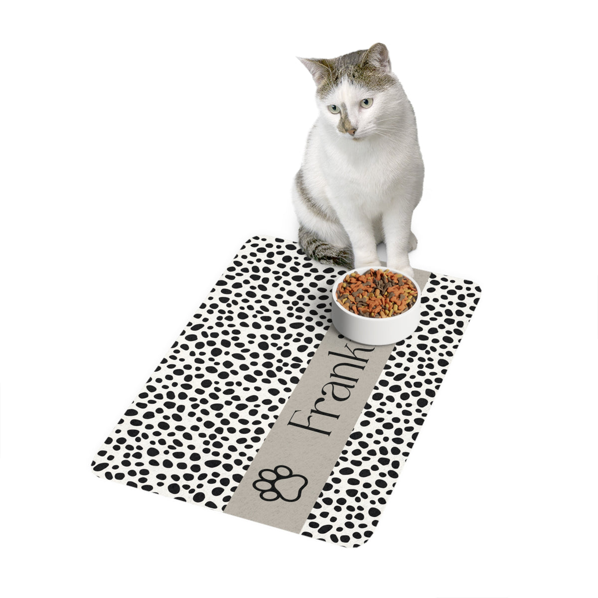 Cat sitting on a spotted paw personalized pet food mat next to a food bowl