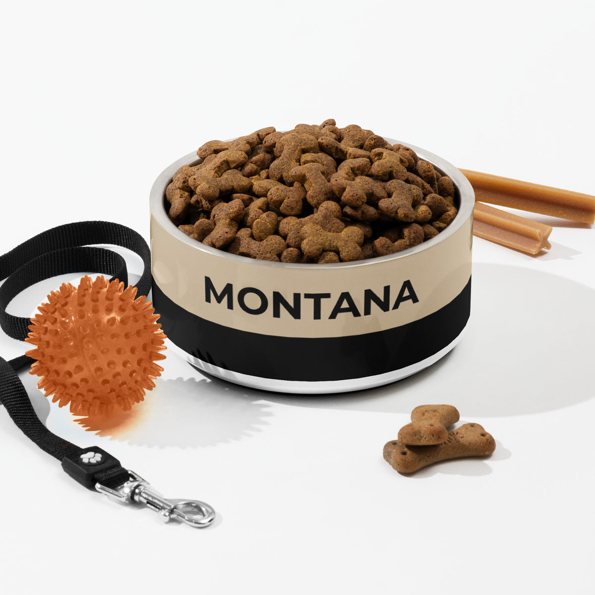 Large tan and black two-tone personalized dog bowl with kibble, a leash, a ball and dog treats