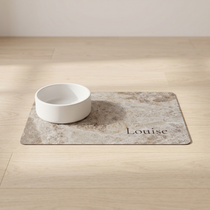 White bowl on a taupe marble personalized pet food mat with the name Louise on a wooden floor
