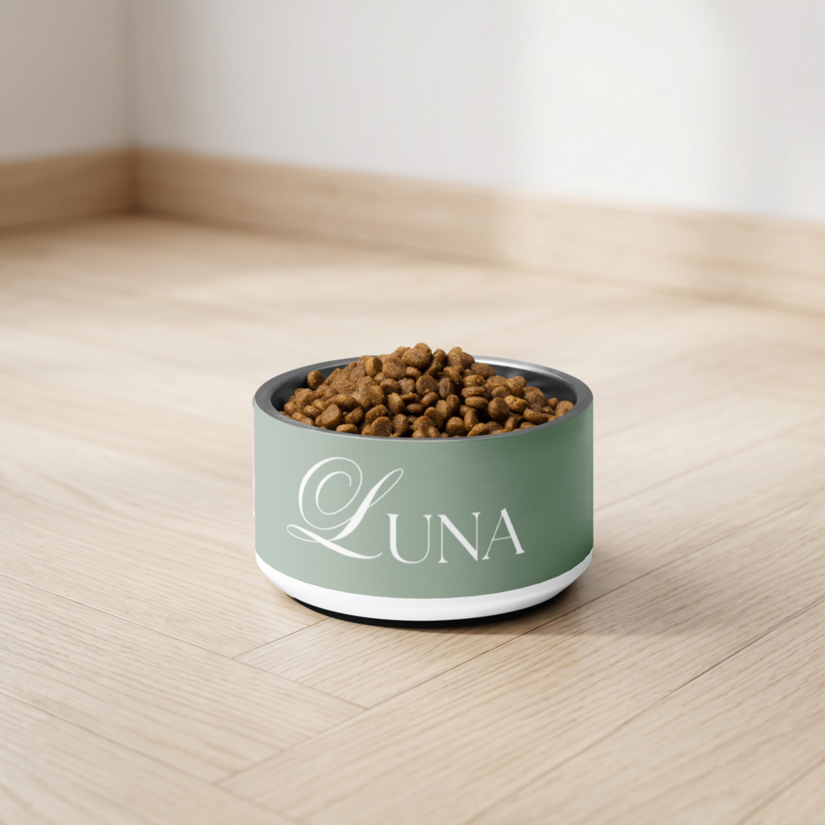 Thyme green personalized dog bowl with kibble on a wooden floor against a white wall