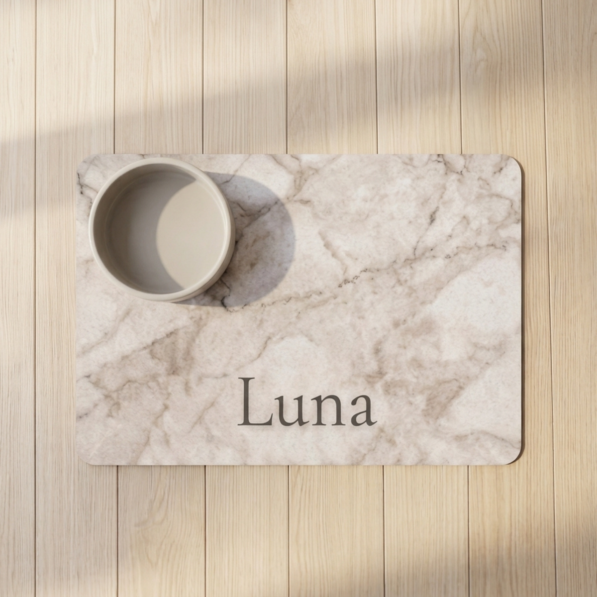 White marble personalized pet food mat with the name Luna and a bowl on a wooden floor